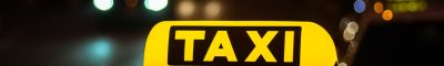 Yellow and black sign of Taxi placed on top of a car at night Yellow and black sign of Taxi placed on top of a car at night